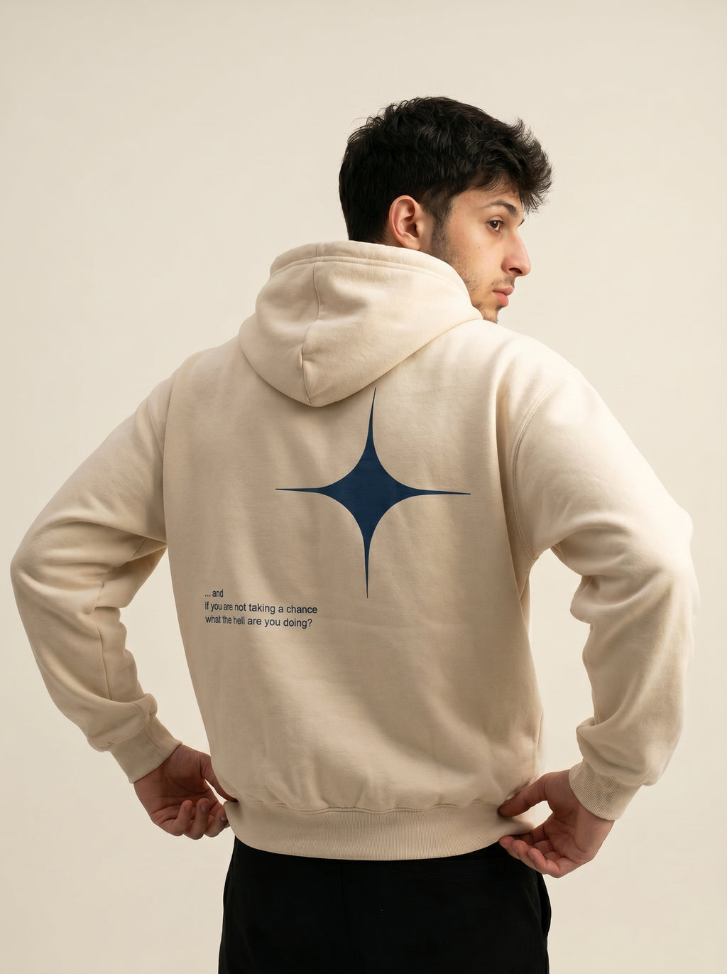Person wearing a beige hoodie with a blue star design on the back against a plain background