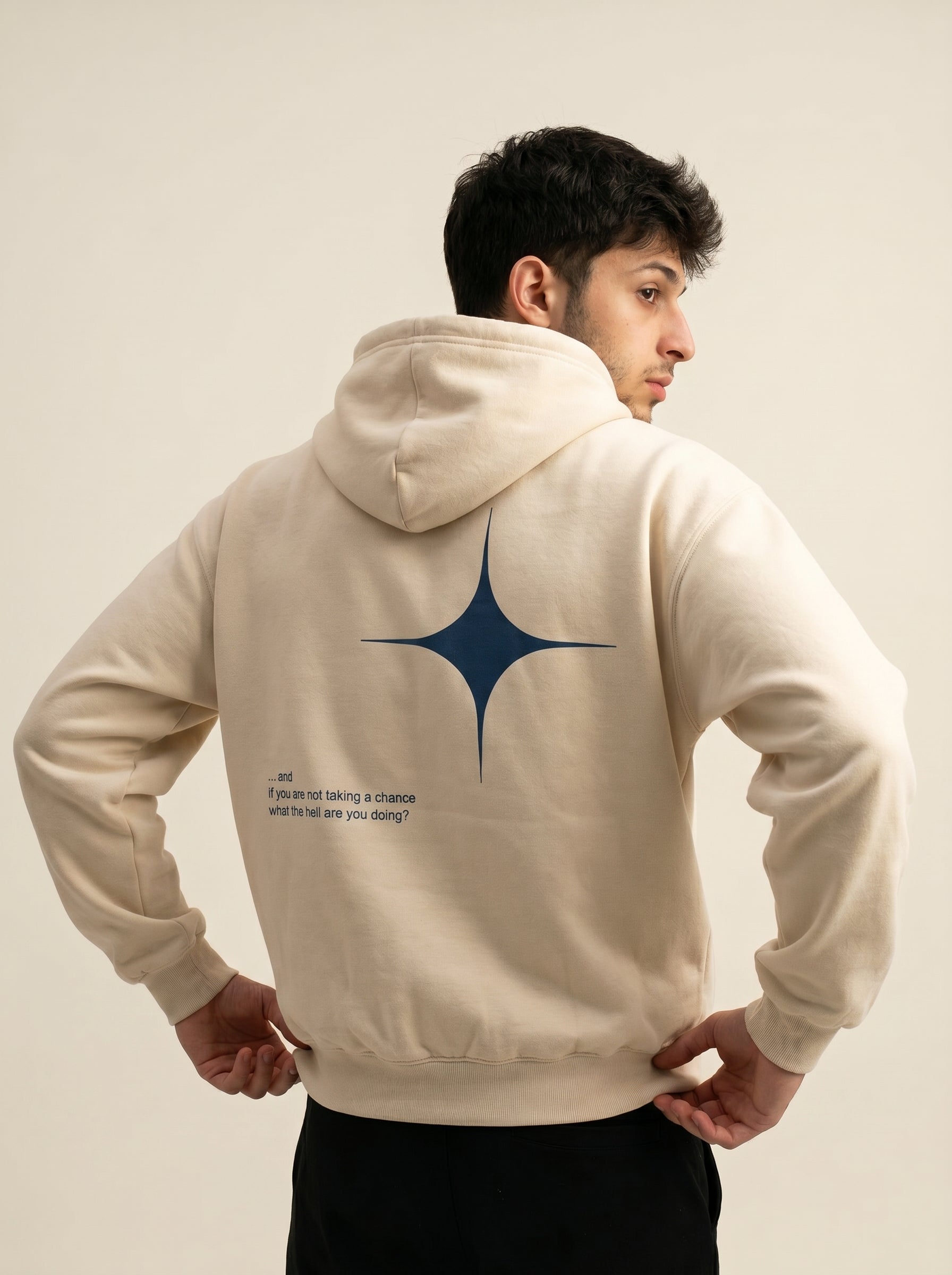 Person wearing a beige hoodie with a blue star design on the back against a plain background