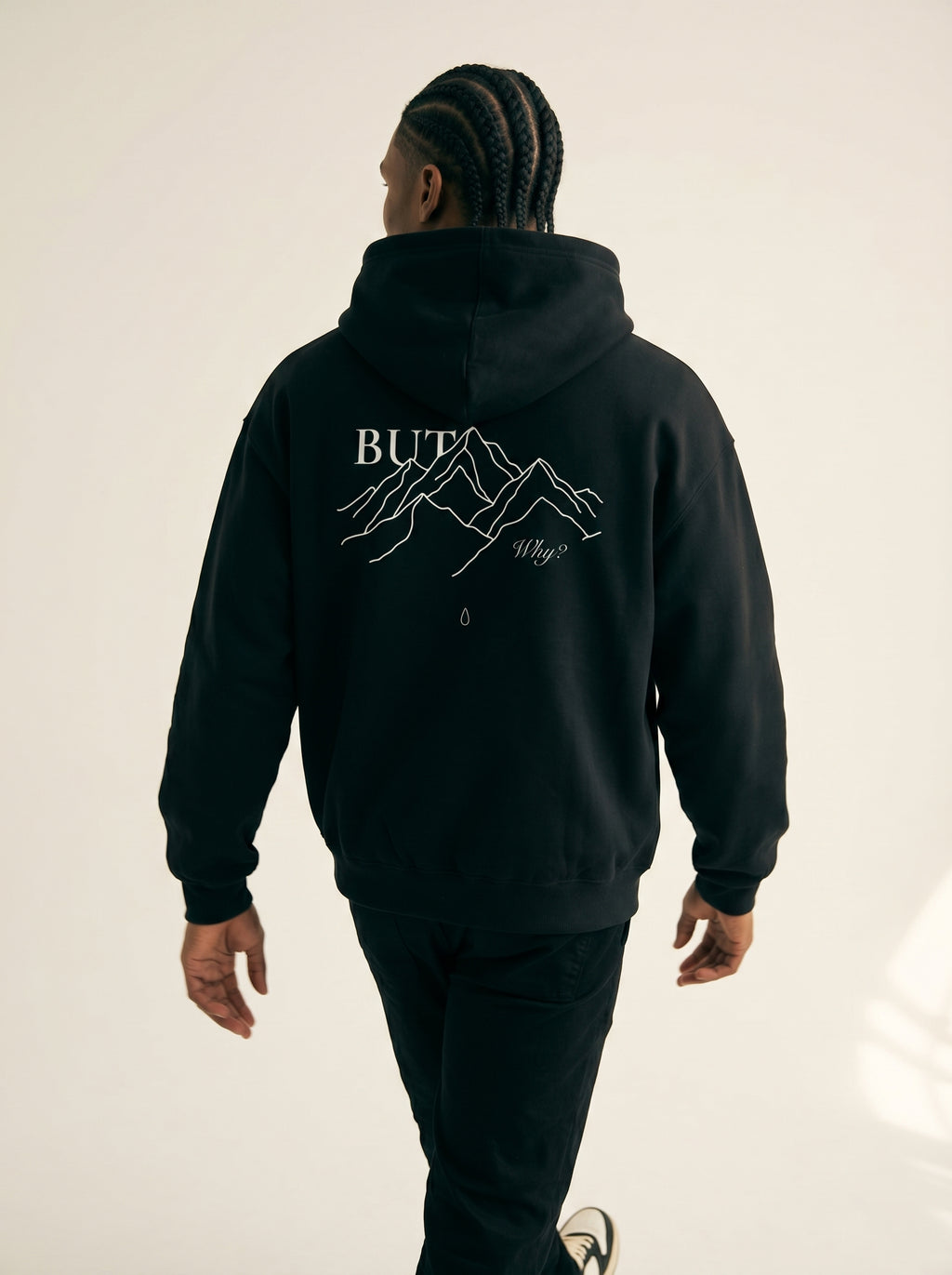 Person wearing a black hoodie with mountain graphic and text on the back, standing against a plain background.
