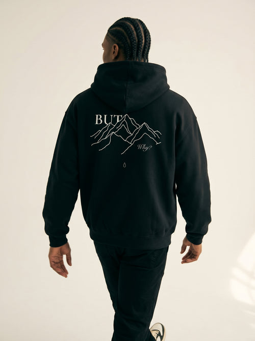 Person wearing a black hoodie with mountain graphic and text on the back, standing against a plain background.