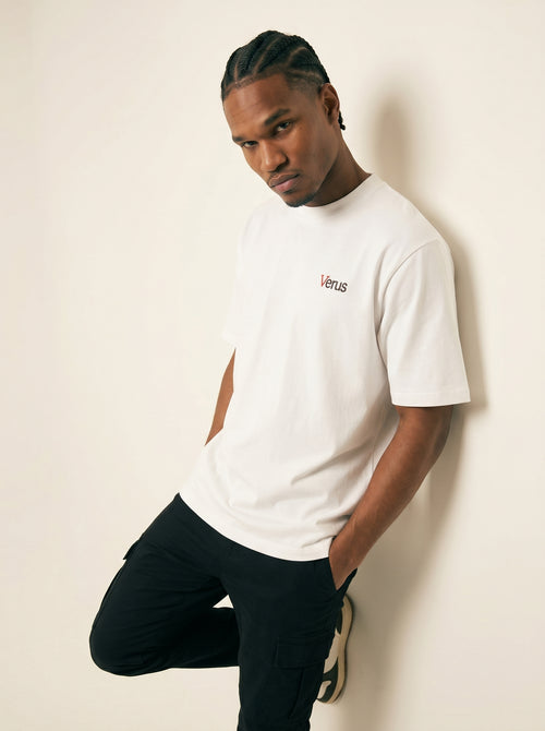 Man wearing a white t-shirt with a logo against a beige wall