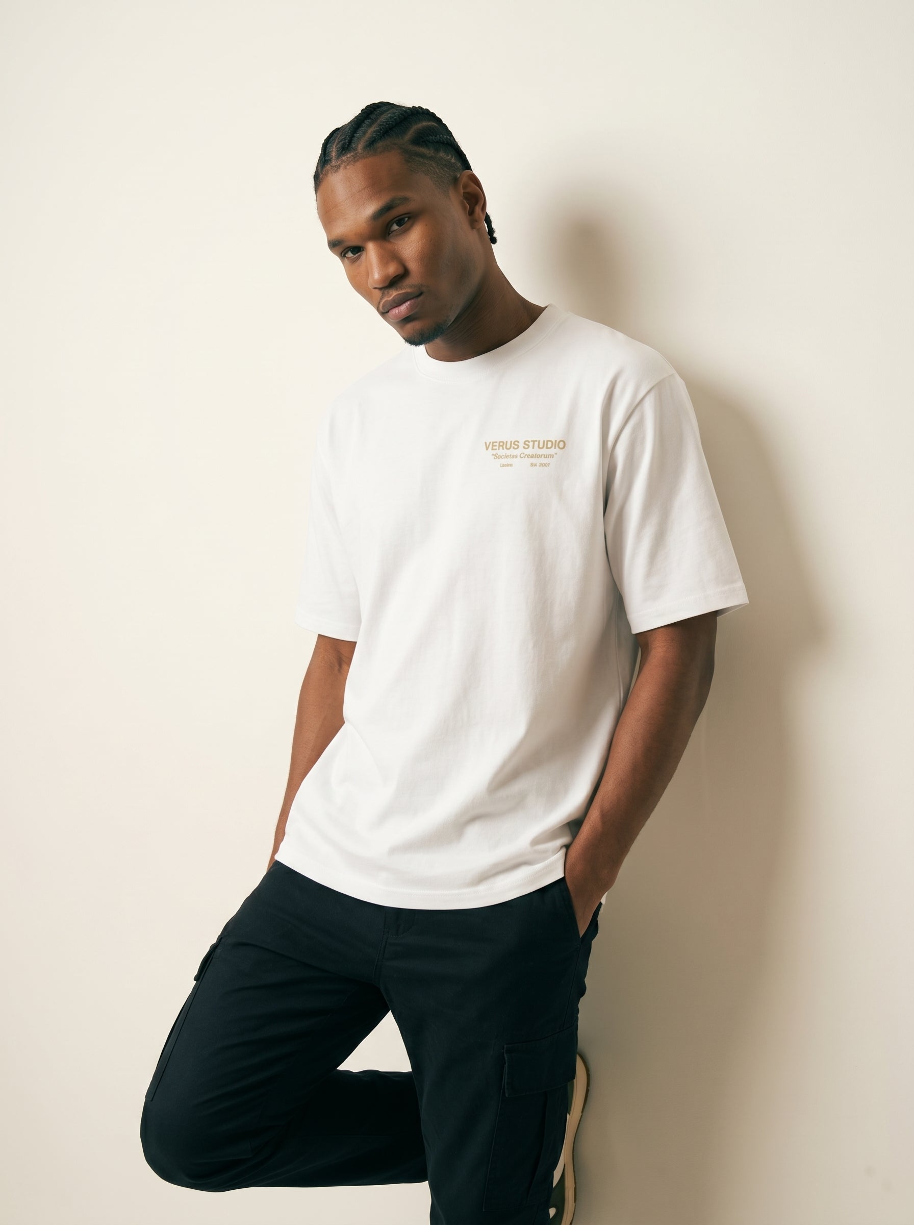 Man wearing a white t-shirt with text and dark pants against a beige background