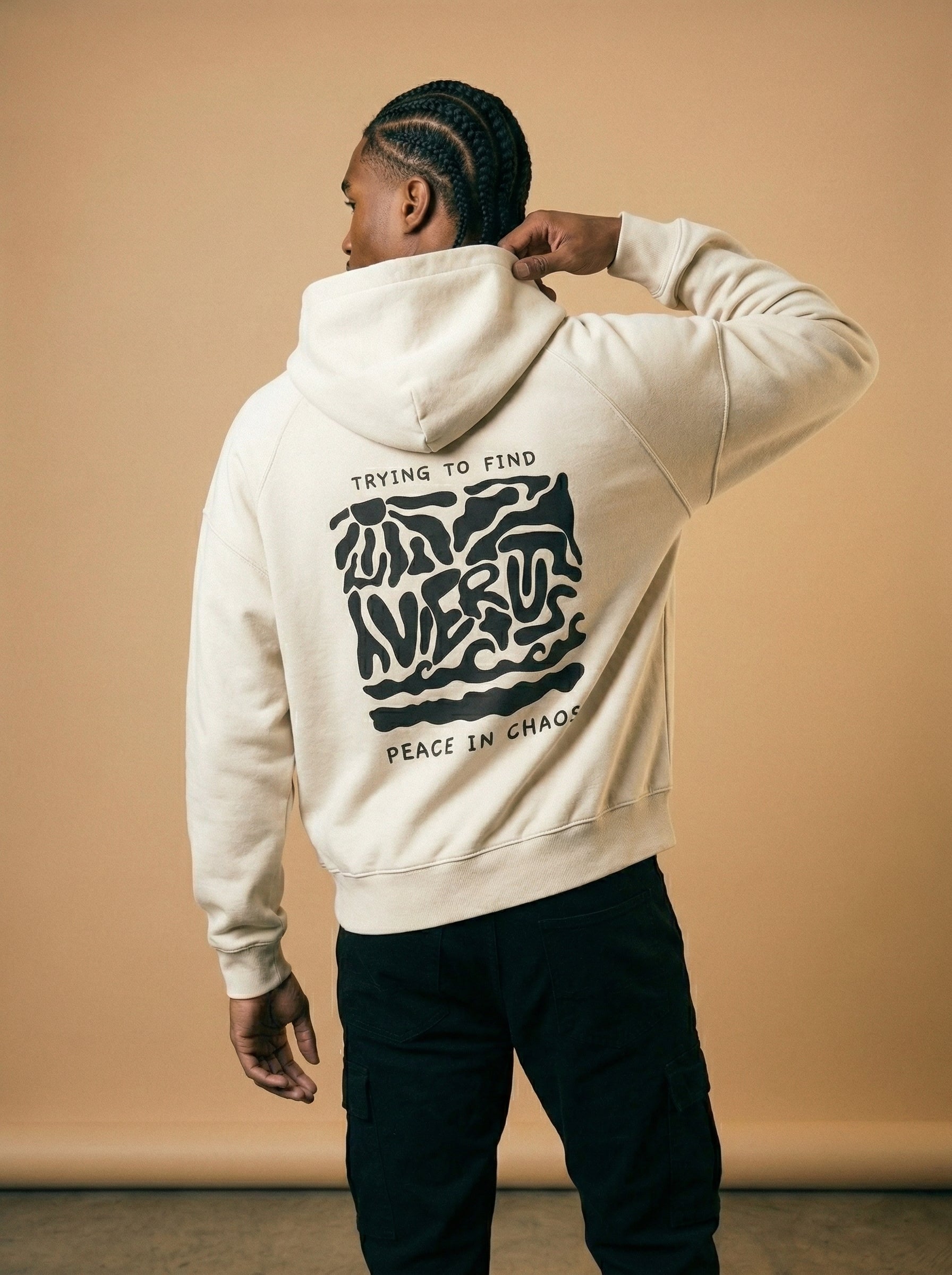 Person wearing a beige hoodie with a black graphic design on the back against a beige background