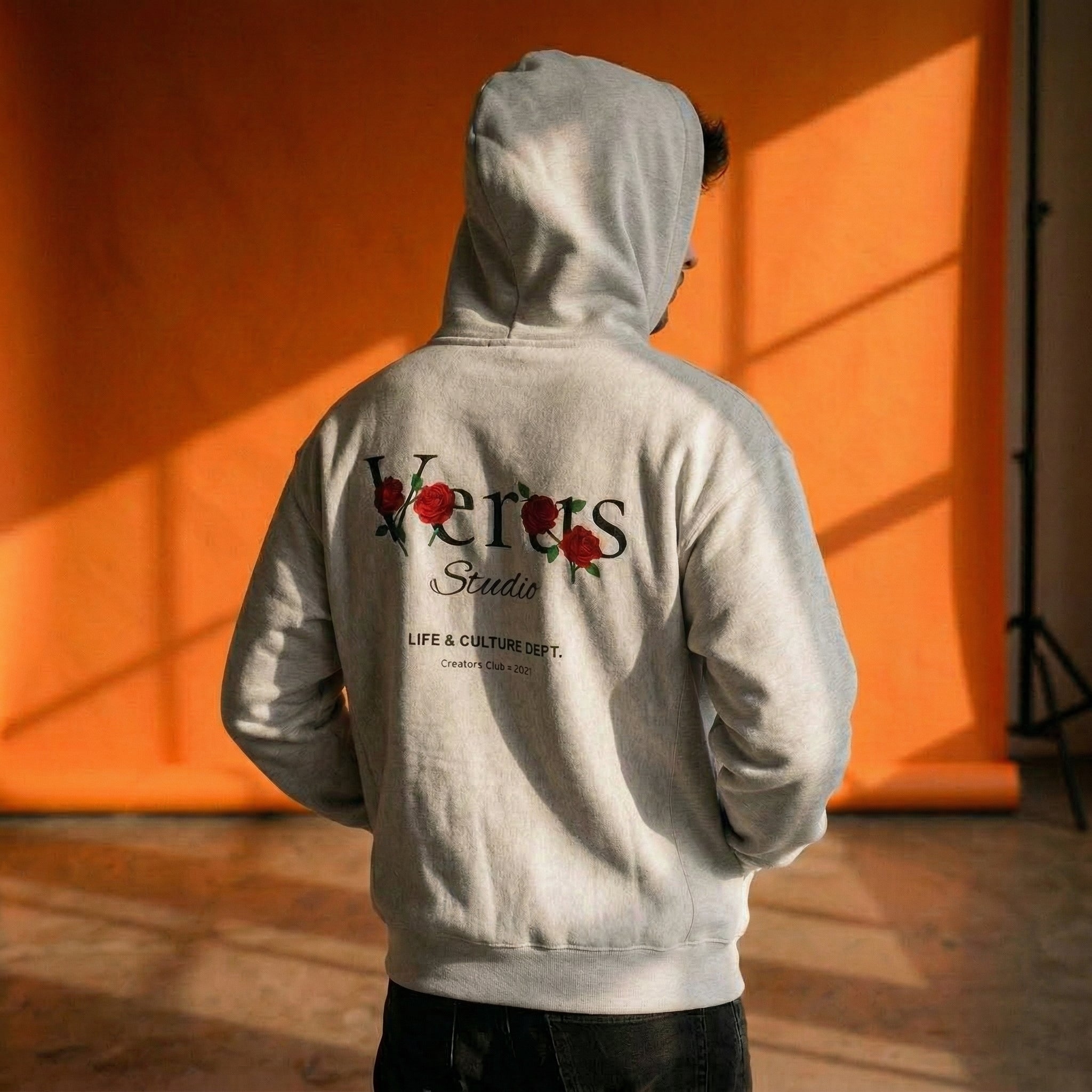 Person wearing a gray hoodie with 'Versus Studio' branding against an orange wall.