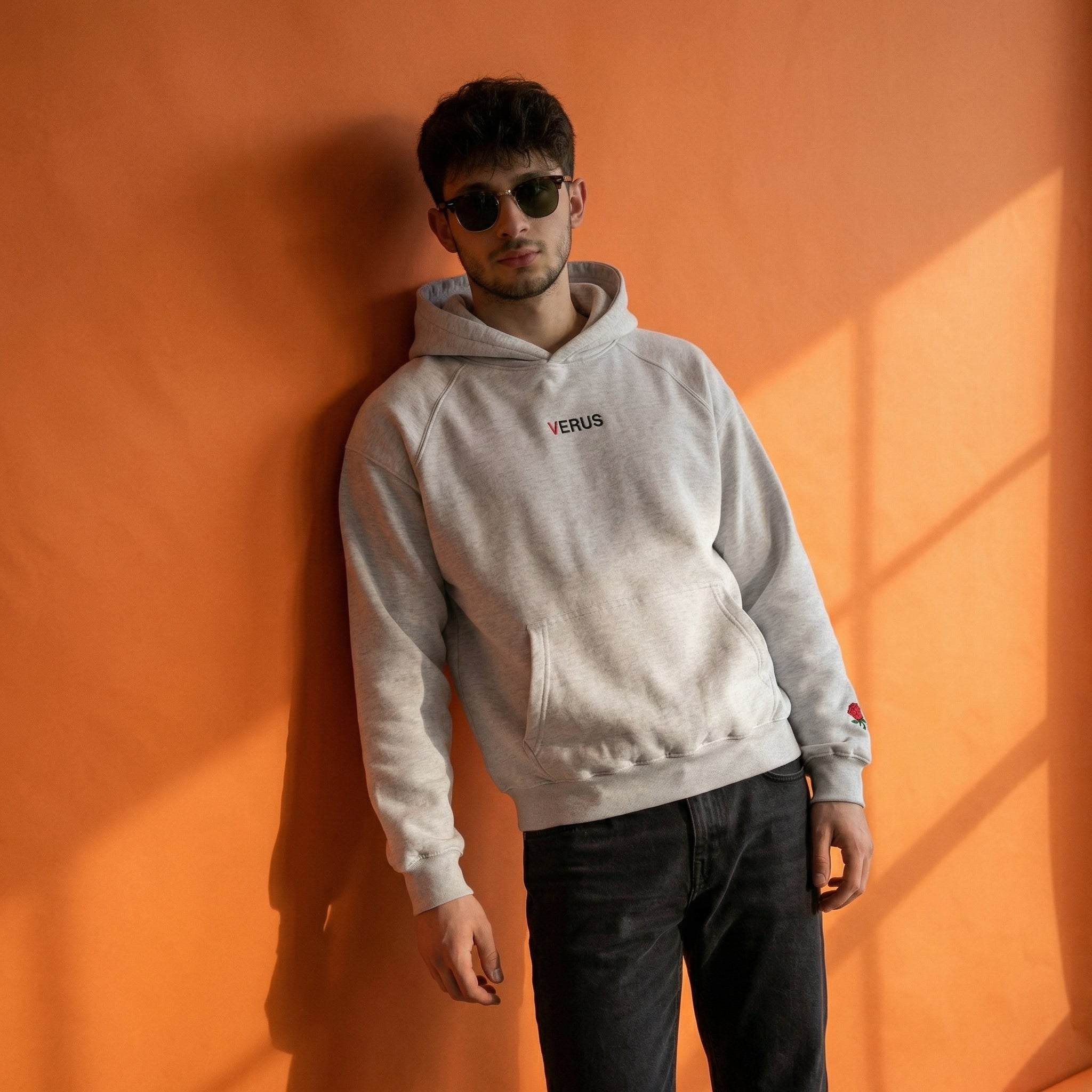 Person wearing a light gray hoodie with 'VERUS' logo against an orange wall