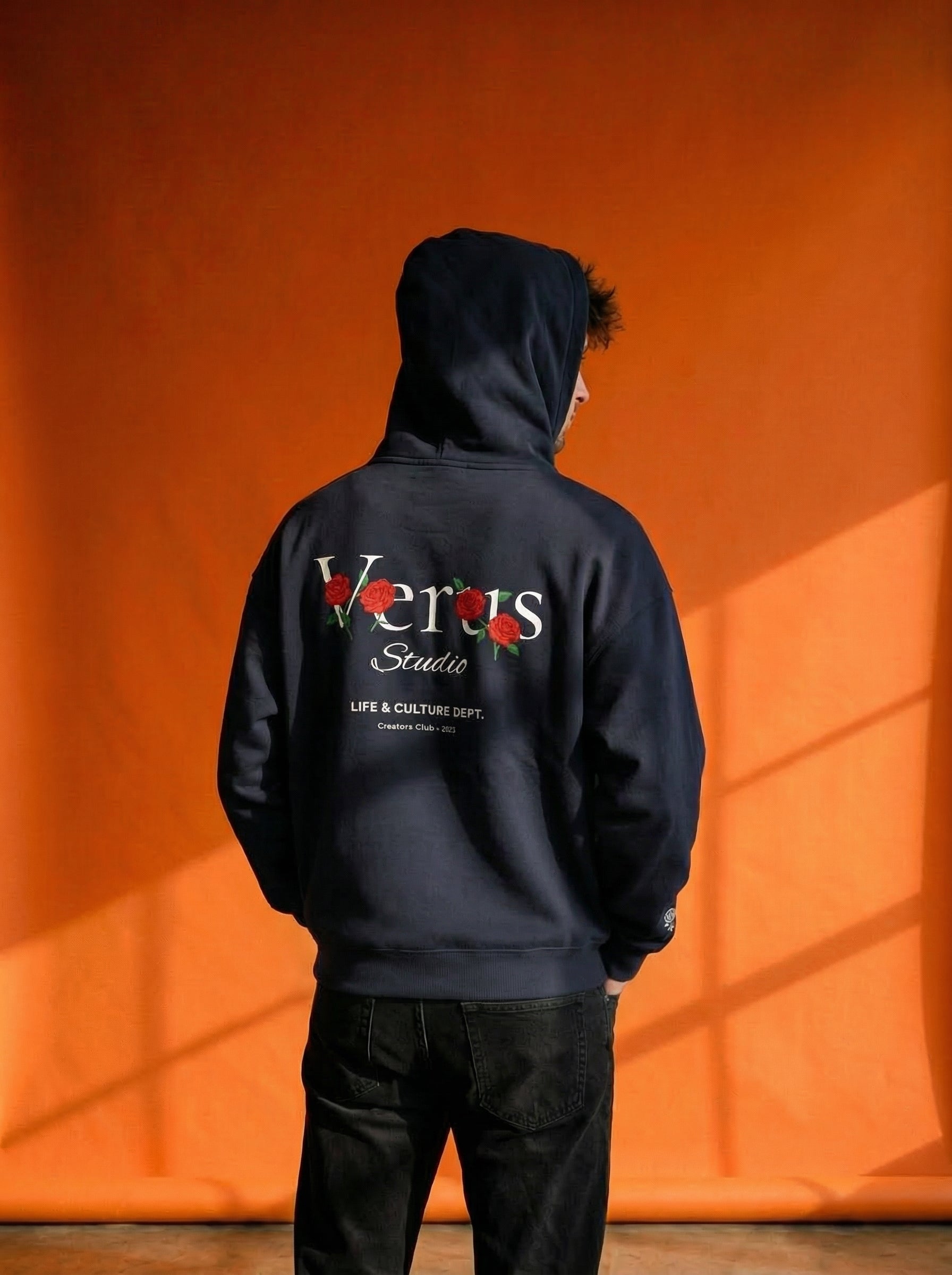 Person wearing a black hoodie with 'Versus Studio' branding against an orange background