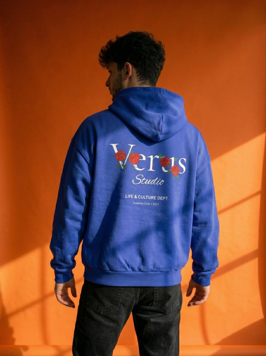 Person wearing a blue hoodie with 'Veras Studio' branding against an orange background