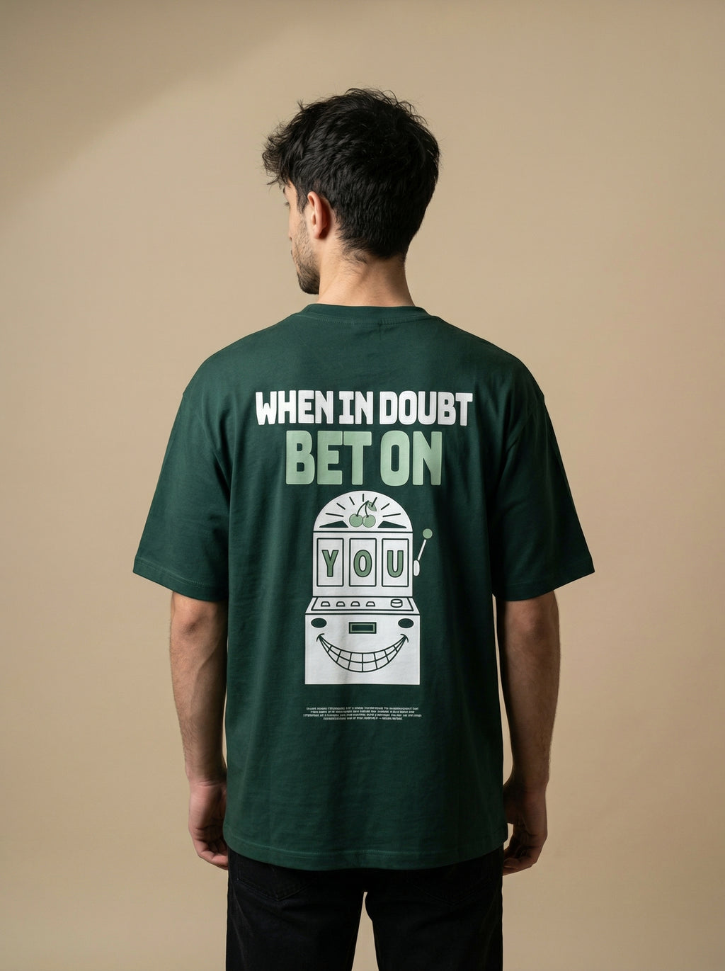 Person wearing a green t-shirt with text and graphic on the back against a beige background