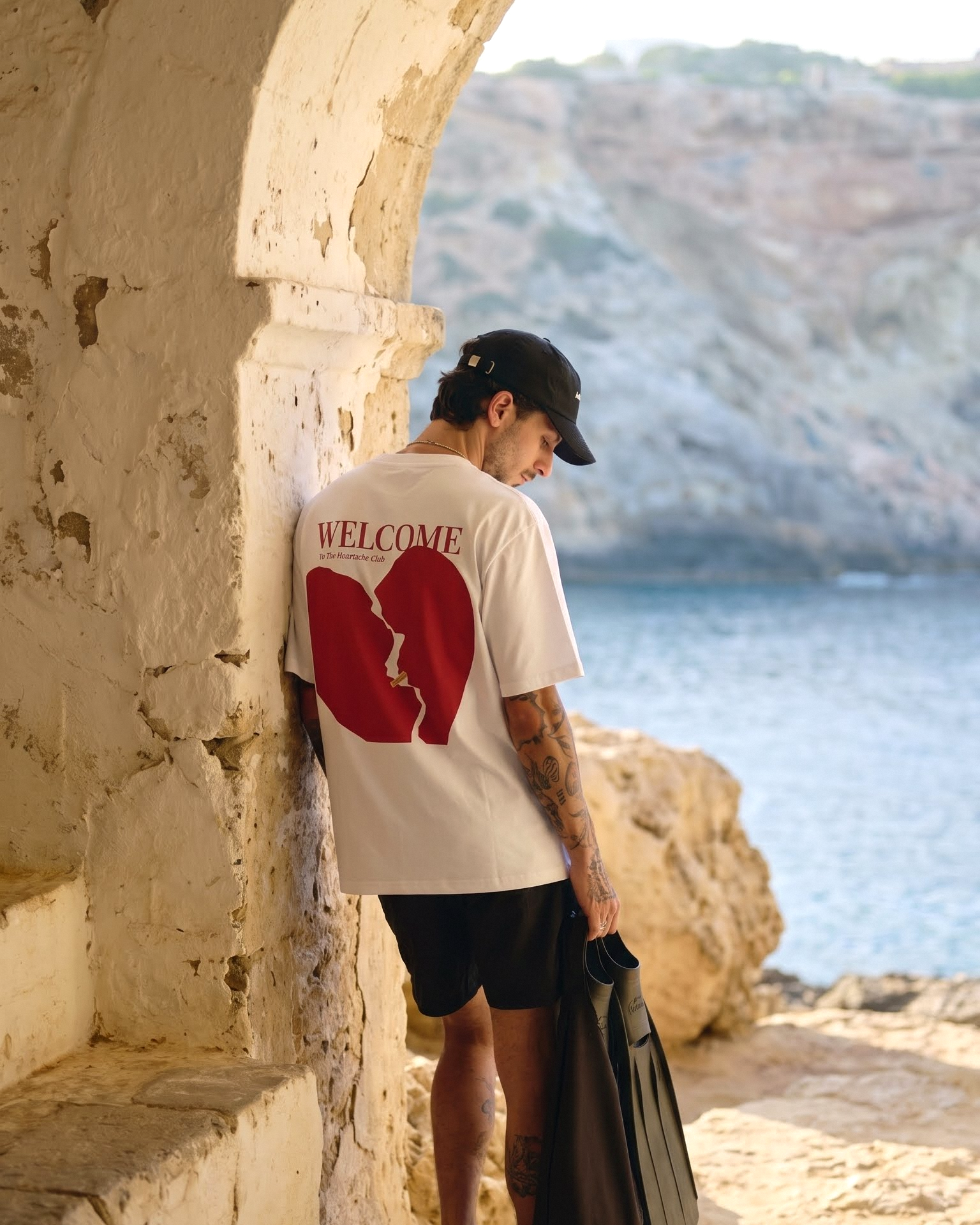 Person standing by a stone archway with a scenic view of water and mountains.